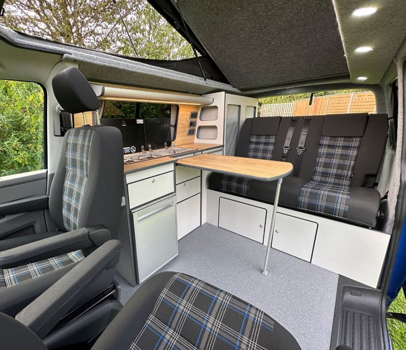 VW campervan interior with grey tartan seating, kitchenette and pop-top roof
